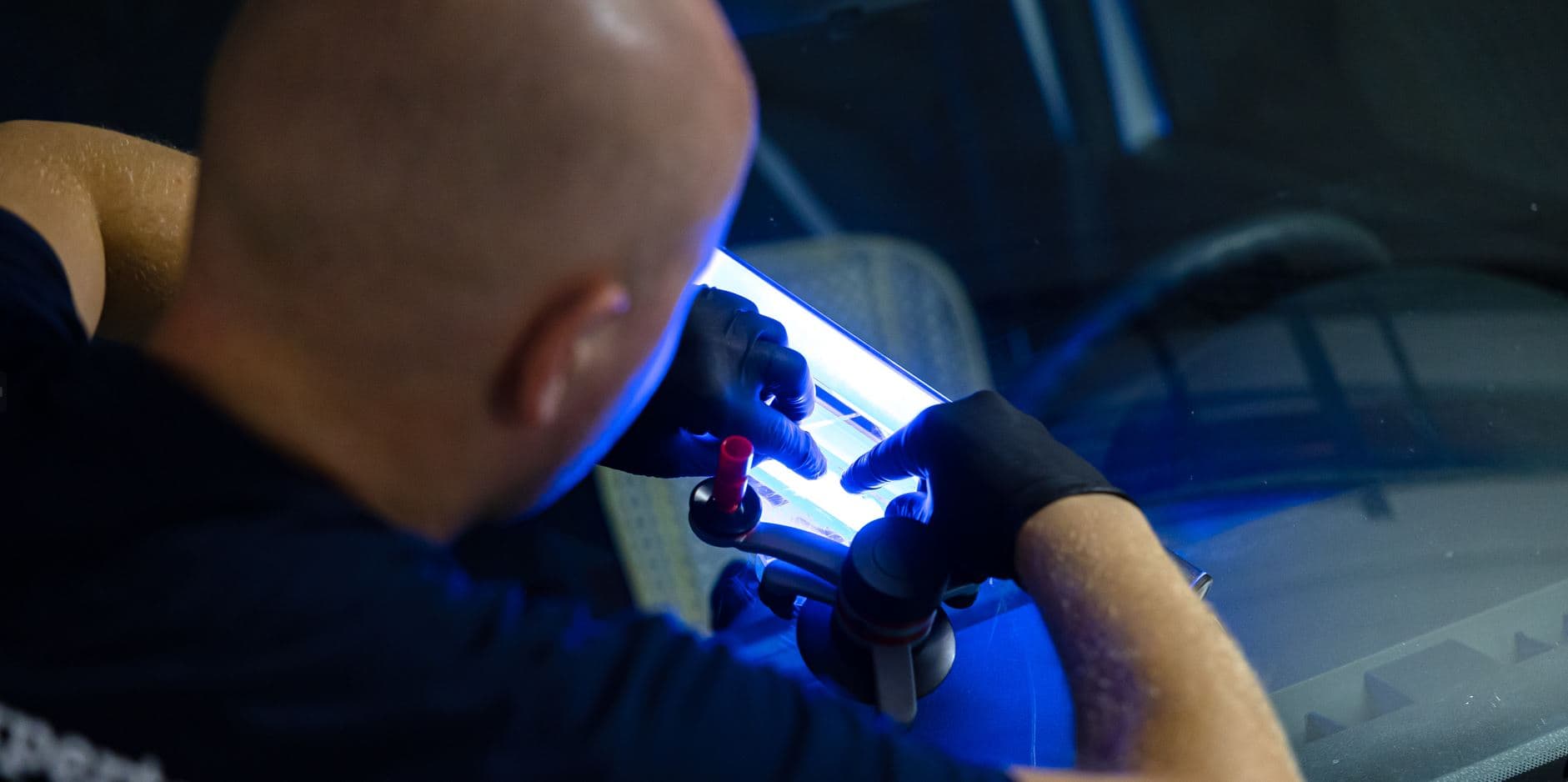 Ein Techniker repariert die Windschutzscheibe eines Fahrzeugs mit einer UV-Lampe